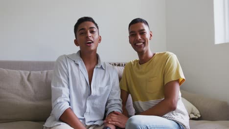 Happy-mixed-race-gay-male-couple-sitting-on-sofa-laughing