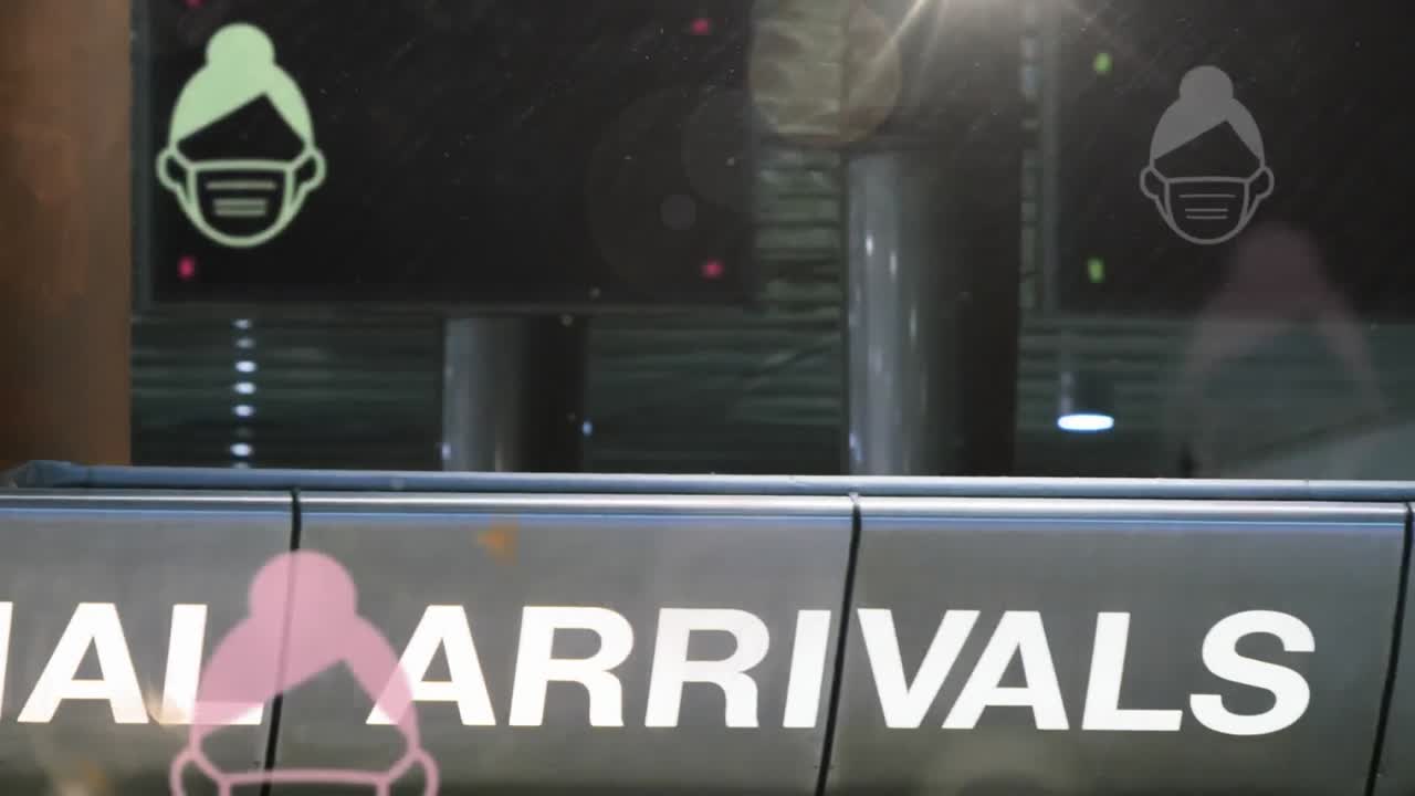video compuesto digital de rostros humanos que llevan iconos de máscara moviéndose contra el aeropuerto en el fondo