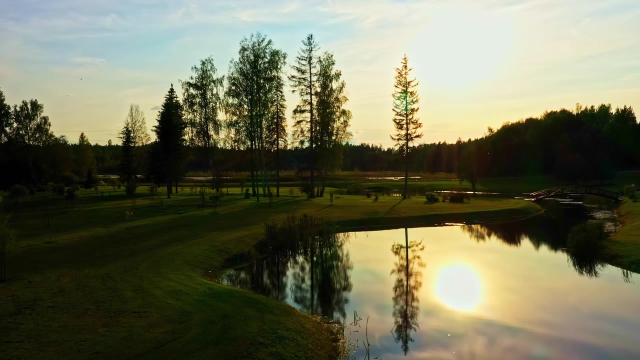 Tramonto che si riflette sull'acqua dello stagno, scenario di un campo da golf verde, vista aerea.
