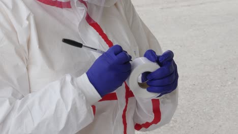 close-up of a medical worker in full protective gear writing labels for coronavirus testing kits during the covid-19 pandemic