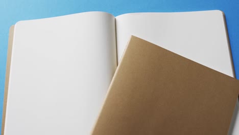 close up of open blank book and brown notebook with copy space on blue background in slow motion