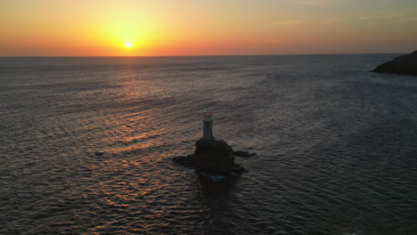 Aerial-view-video-of-iconic-lighthouse-in-Andros-island-chora,-Cyclades,-Greece-at-dusk