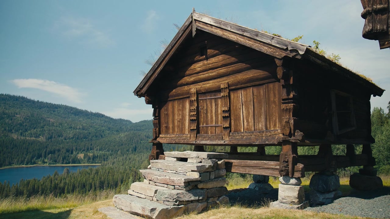 Tradisjonelt norsk stabbur med torvtak, med utsikt over en skog og en innsjø, som viser nordisk kulturarv, historisk arkitektur og landlig kultur