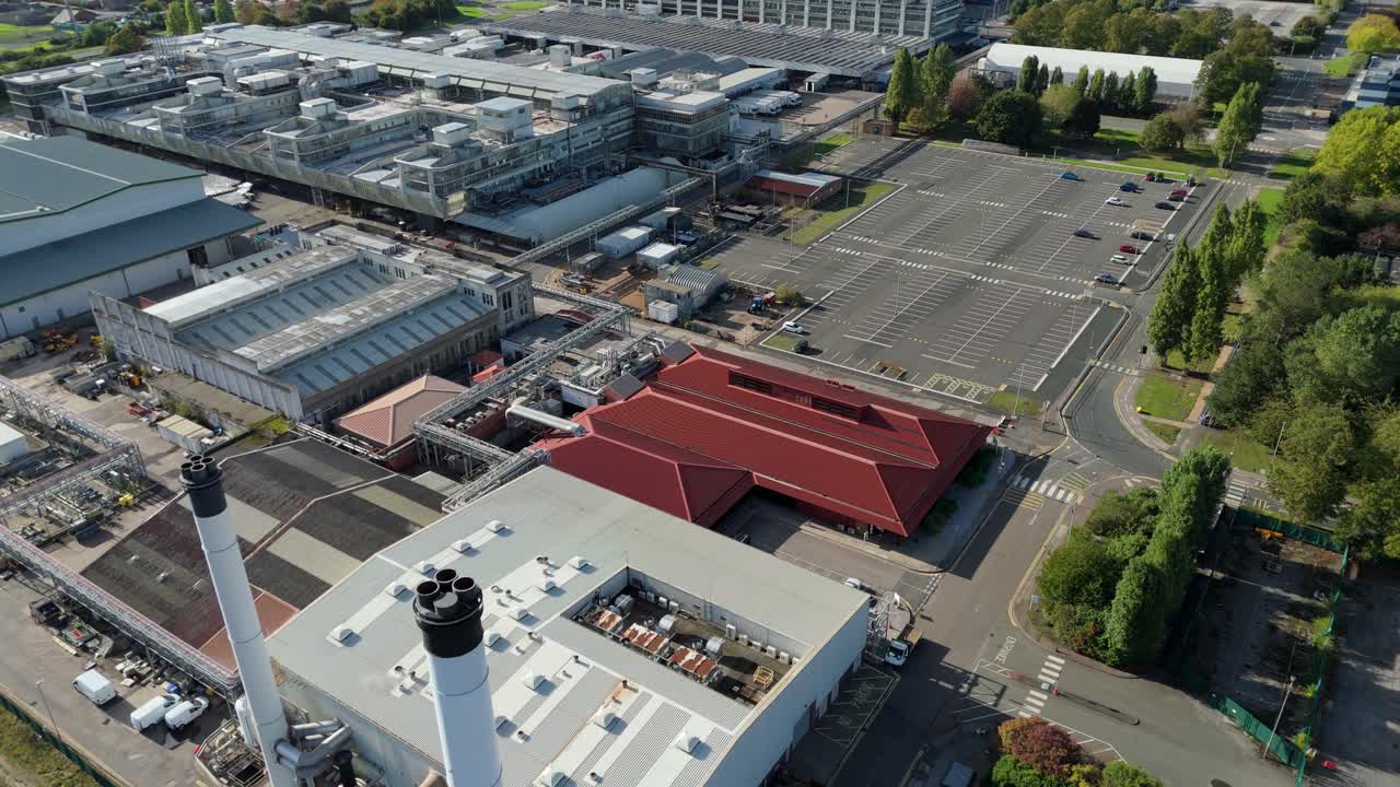 Tracking drone shot of factory roofscape, piping networks, chimneys and parked heavy machinery in Nottingham UK industrial zone