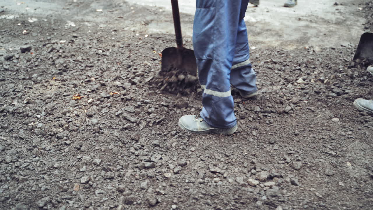 Legs of workers in protective uniform and boots with shovels leveling up the road. Team of workers preparing the ground for making new asphalt on a street. Close-up