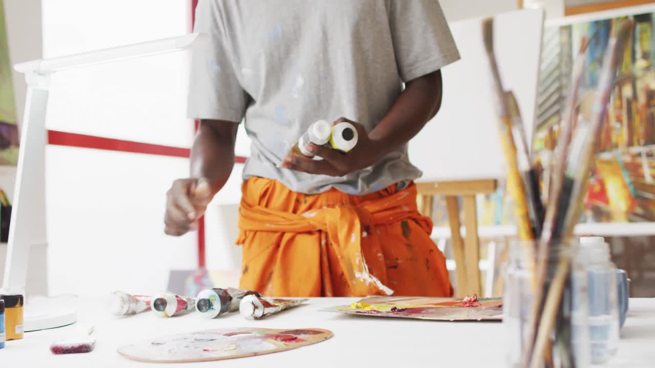 Midsection of african american male painter choosing paint in artist studio
