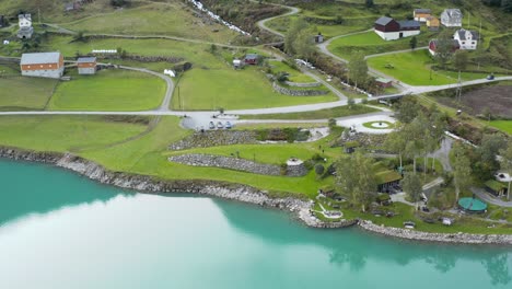 Aerial-View-of-Village-and-Green-Landscape-by-Glacial-Fjord-Lake-Water,-Norway