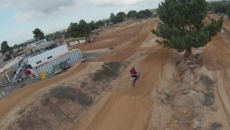 fpv aéreo en cámara lenta alrededor del árbol revela a los pilotos de motocross en una pista de tierra siguiendo al piloto