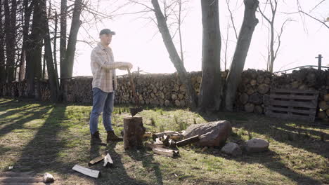 caucasian man leaning on an ax resting after chopping wood outside a country house