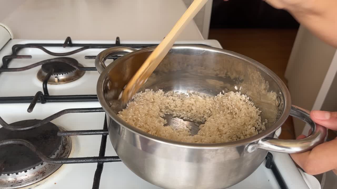 preparación del arroz, se fría en una olla de acero, el cocinero lo agita con una cuchara de madera