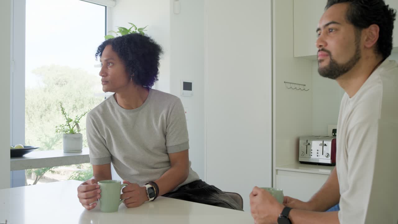Men sitting at kitchen island, reacting to woman speaking while holding green mugs, phone appearing
