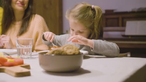 blonde little girl eating apple pie sitting at the table while her parents talking during dinner at home