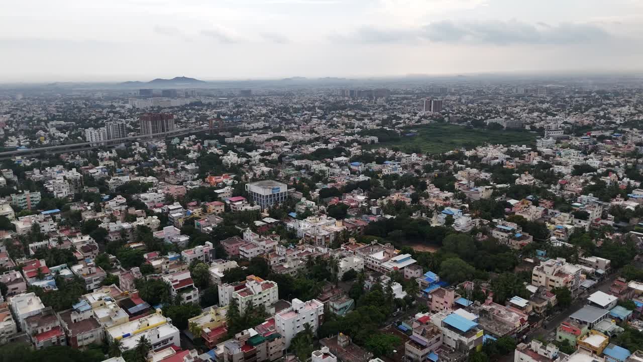 A sweeping aerial view of a vast urban landscape. Shot during a late-afternoon drizzle, the footage captures the raw energy and high population density of a bustling city
