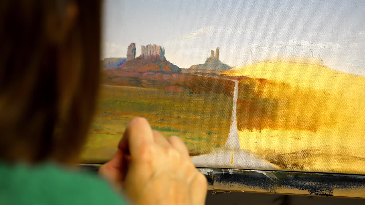 Inquadratura media della mano delicata di un artista che aggiunge dettagli a un dipinto a olio della Monument Valley.