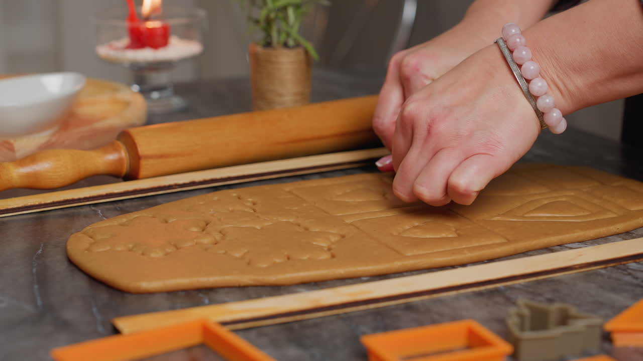primer plano de una mujer usando un cortador cuadrado naranja en la masa, formando cuadrados limpios, rodillos y otras herramientas de horneado son visibles cerca en la encimera de mármol