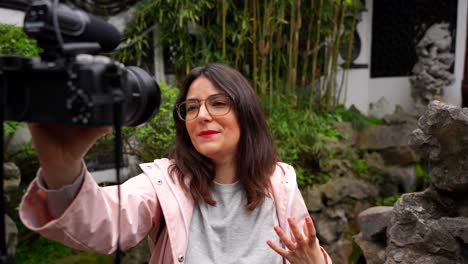 mujer filmándose a sí misma hablando con una cámara profesional en el jardín de yuyuan, china