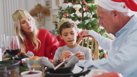 Sohn-Spielt-Mit-Weihnachtscracker-Neuheitsgeschenk-Und-Sitzt-Mit-Mutter-Und-Großvater-Am-Esstisch