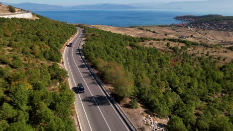 Cars-and-bus-driving-on-panoramic-curved-road-with-blue-lake-background-in-Albania