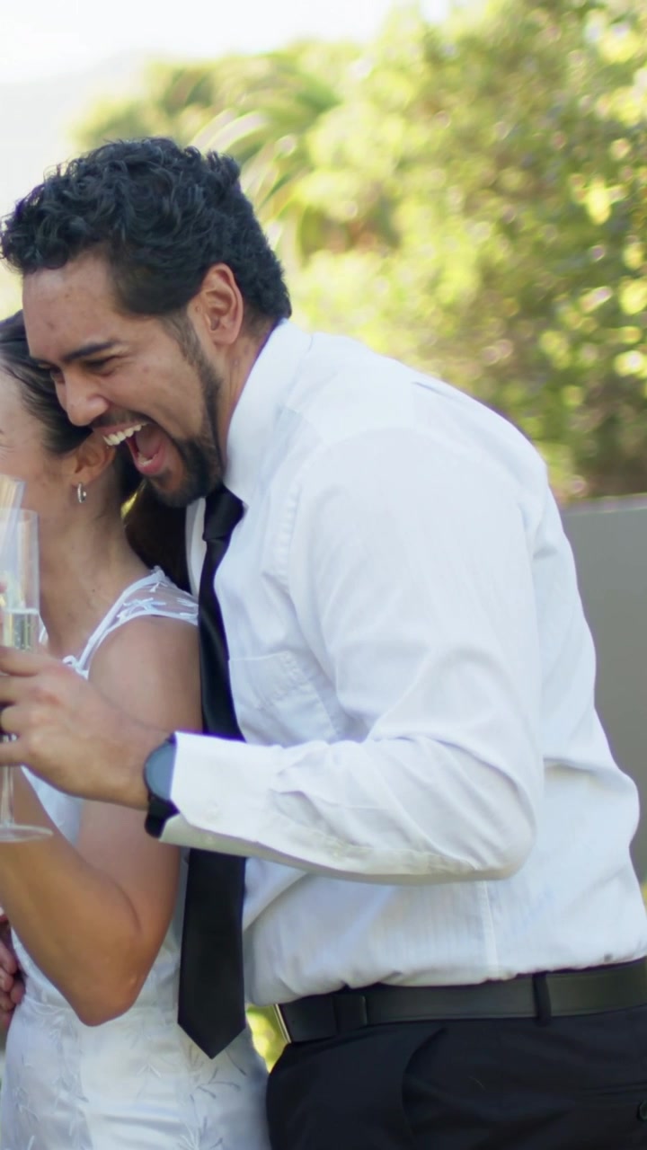 Video vertical: Hombre apoyado con camisa y corbata riendo, levantando copas para brindar en el jardín