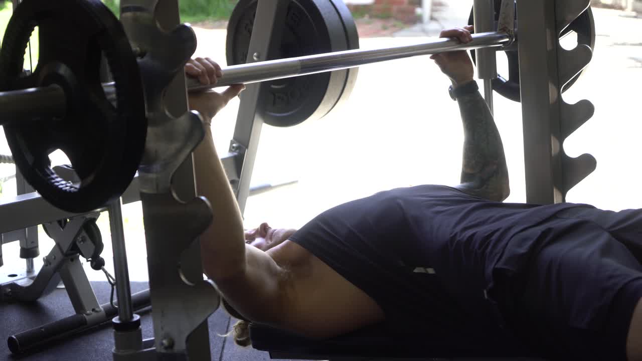 hombre tatuado en el gimnasio en casa máquina smith press de banca hombre