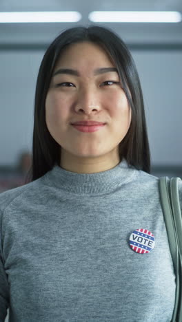 woman stands in a modern polling station, poses, smiles and looks at camera. portrait of muslim woman, united states of america elections voter. background with voting booths. concept of civic duty.