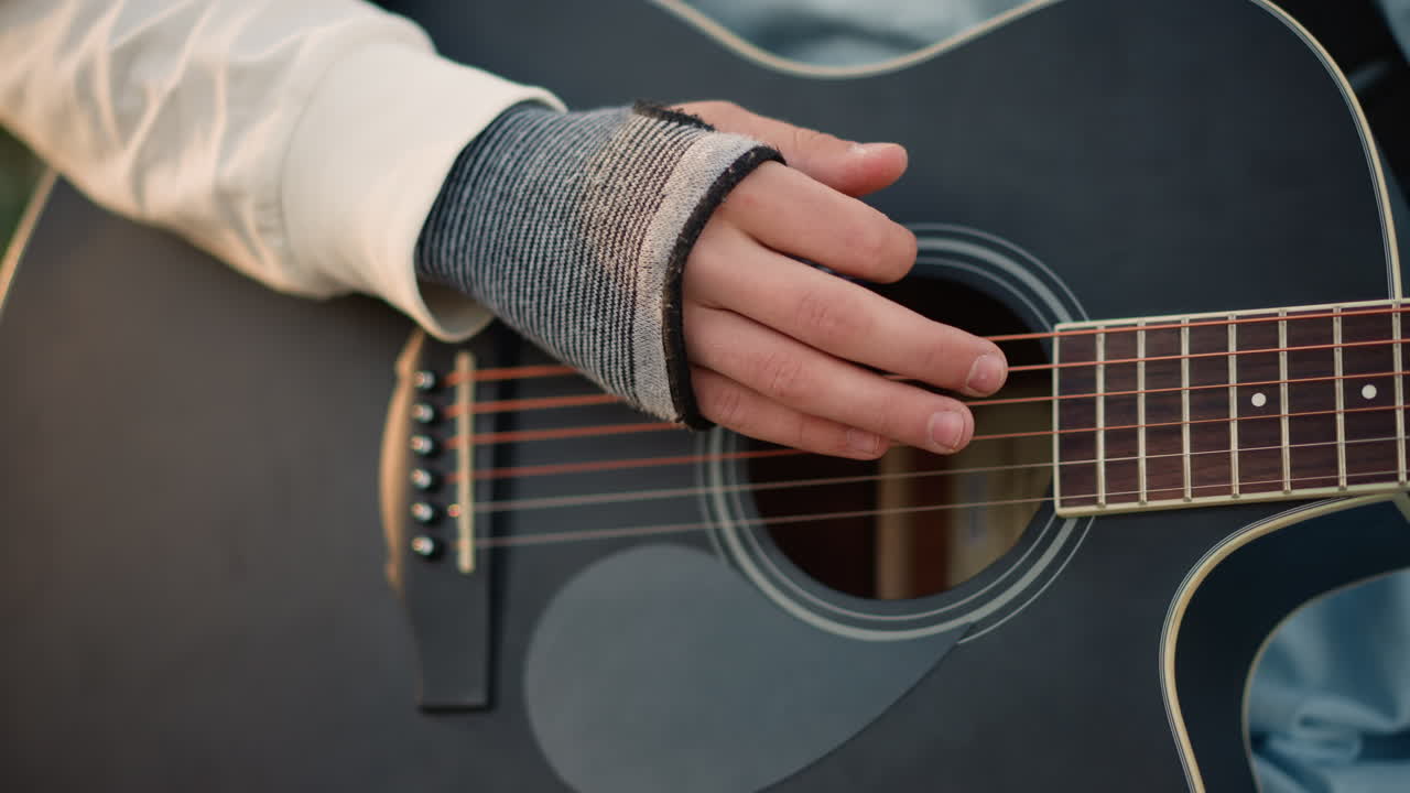 primo piano delle mani sulle corde della chitarra, dettaglio dei guanti senza dita, polpastrelli agili che pizzicano, plettrata e tono precisi, tastiera e battipenna visibili, texture tattile e dettaglio dei calli, acustica intima