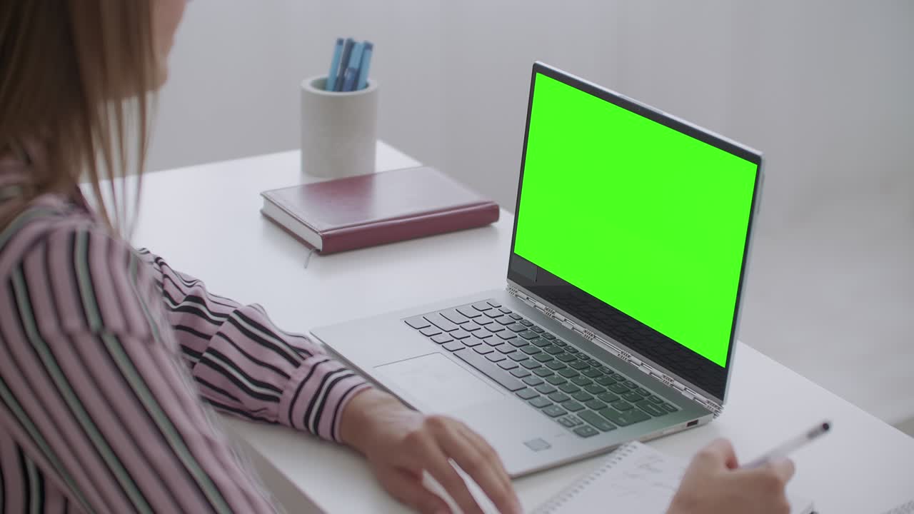 e-educación, la mujer está viendo en la computadora portátil con pantalla verde para la tecnología chroma key, la estudiante está escribiendo notas