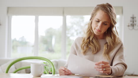 worried woman sitting at table at home reviewing domestic finances opening letter with bill