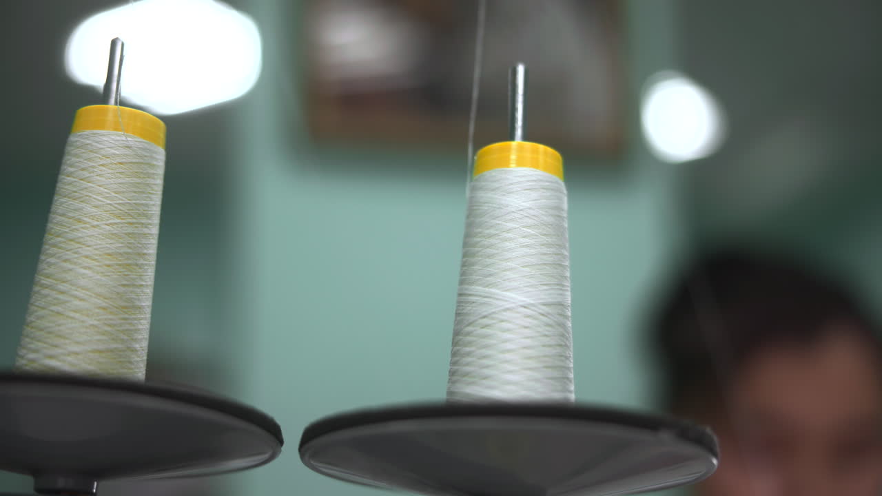 Closeup Spools Of White Thread On Industrial Sewing Machine, Blurred Seamstress In Background, Soft Studio. Media