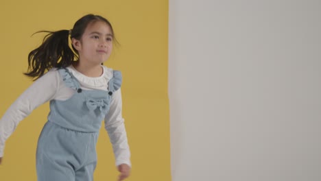 studio portrait of hyperactive girl jumping and spinning against yellow and white background