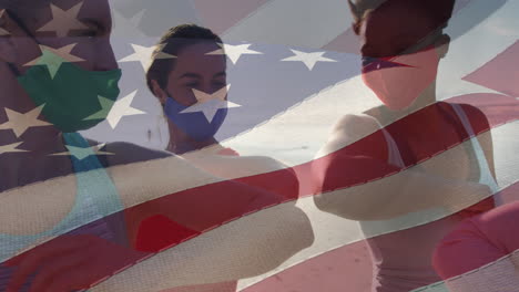 animation of flag of united states of america over people in face masks on beach