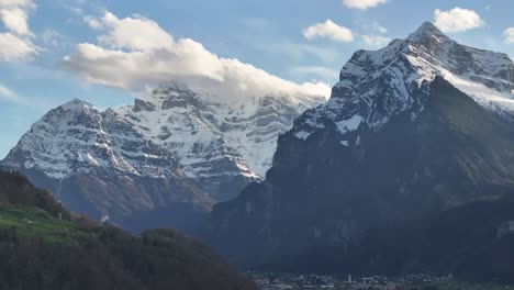 Majestic-Aerial-view-of-Vorder-Glärnisch,-Wiggis,-and-Rautispitz-in-Glarus-Nord,-Switzerland,-towering-over-a-quaint-village