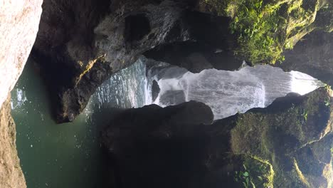 Cámara-Vertical-Lenta-Inclinada-Hacia-Arriba-De-Rocas-Divididas-Con-Un-Pequeño-Río-Con-Una-Gran-Cascada-En-El-Paraíso-Tropical-De-Bali-Indonesia