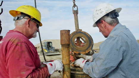 mature men wearing protective helmets stand at the equipment for drilling oil. worker presses the metal detail into the round reservoir.