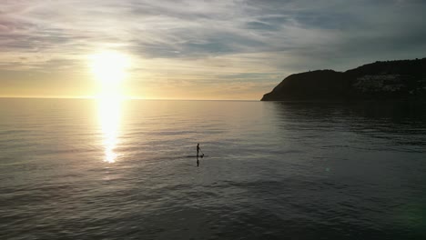 silueta de un hombre adulto parado en el remo de la tabla sup durante la puesta de sol en españa