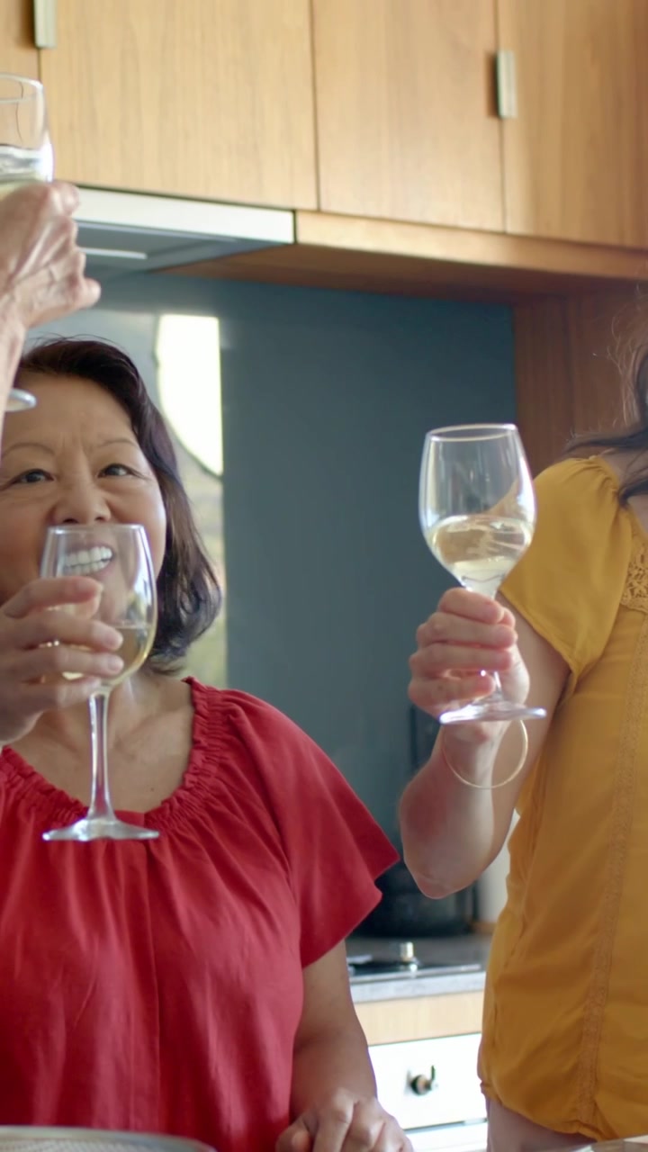 Vertical video: Lifting women in red and yellow blouses clinking wine glasses, toasting in kitchen