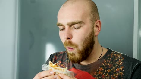 young man eating tasty sandwich, standing indoors