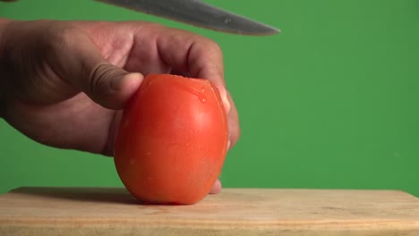 a hand slicing through a tomato on a chroma background