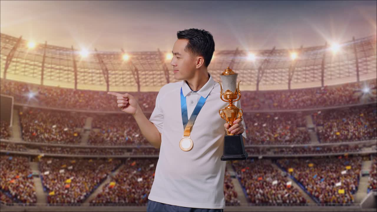 hombre asiático con una medalla de oro sosteniendo un trofeo de oro en sus manos y señalando a un lado en el estadio