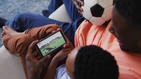 composite of father and son at home watching hockey match on smartphone