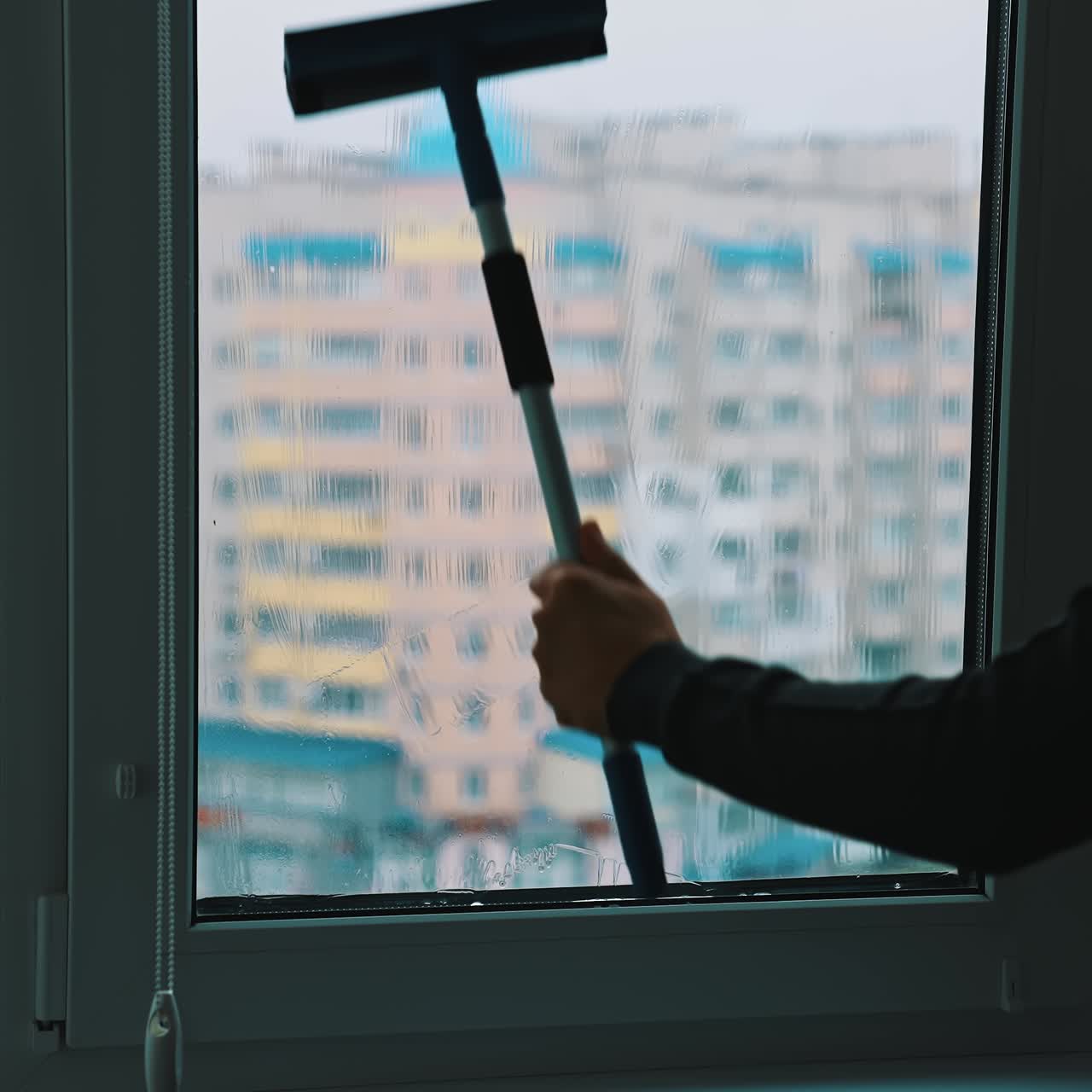 Worker washing plastic window. Man cleaning window with a brush inside the high building in the city. Washing glass window