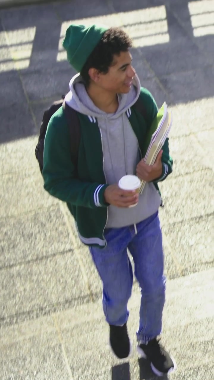Video verticale: Due studenti con berretto camminano, portando caffè e quaderni, diretti a lezione.