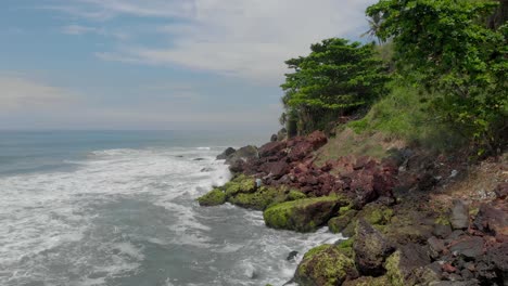 4k-Aerial-Drone-Reveal-shot-of-a-beautiful-27-year-old-young-Indian-woman-in-a-White-and-Blue-floral-dress-standing-alone-on-top-of-a-cliff-enjoying-the-serenity-by-herself-near-the-Seashore