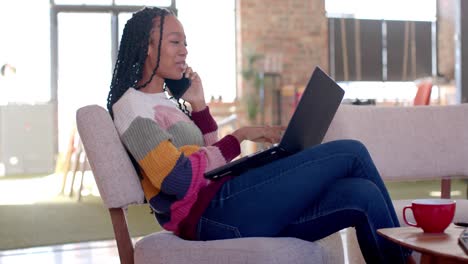 Feliz-Mujer-De-Negocios-Informal-Afroamericana-Usando-Una-Computadora-Portátil-Y-Hablando-Por-Teléfono-Inteligente-En-La-Oficina