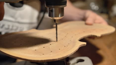 a violin maker is drilling holes to prepare a violin piece