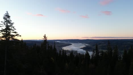 Drone-flying-trought-forest-and-over-shelter-revealing-town-and-river-right-before-sunrise