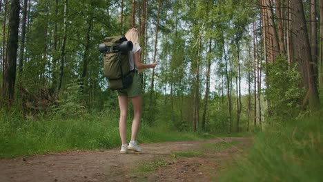 slow motion back view: young caucasian woman looking for direction on a map while hiking in the forest. happy girl while hiking in nature and orienteering with help of a map