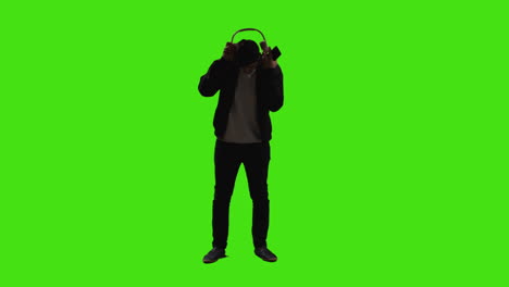 man putting on wireless headphones and streaming music from mobile phone against green screen with low key lighting 2