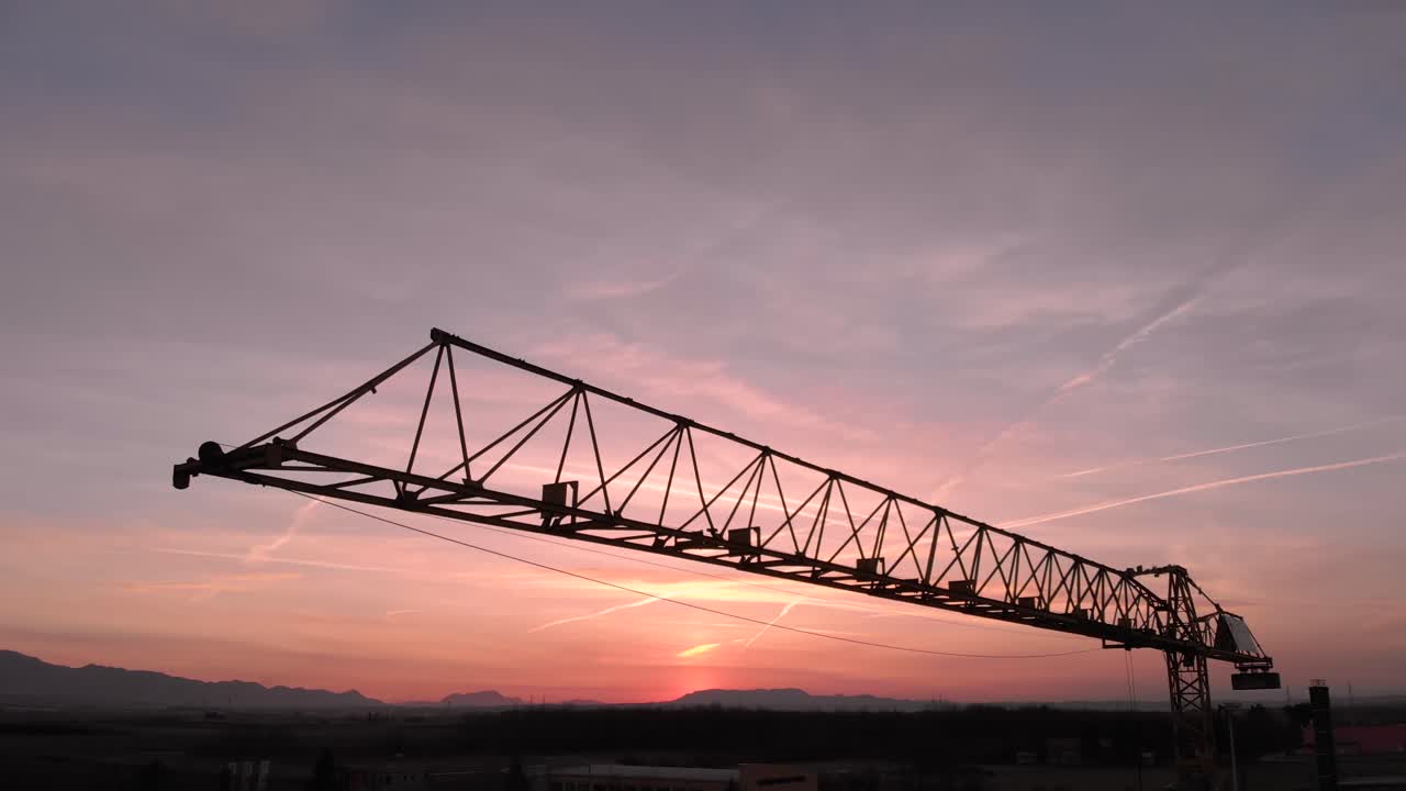 Close up during colorful sunset of Tower crane, big excavator silhouette in a construction site. Aerial drone view