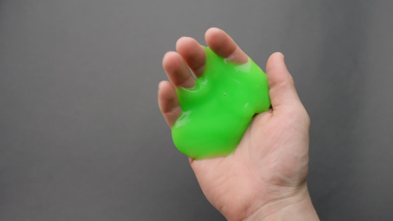 Green slime slowly oozing through fingers in a close-up of a hand indoors